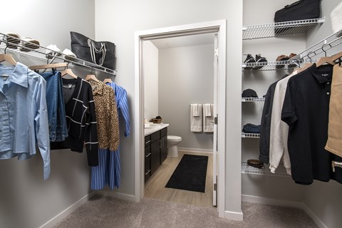 A walk in closet with clothes hanging and shelves with shoes.
