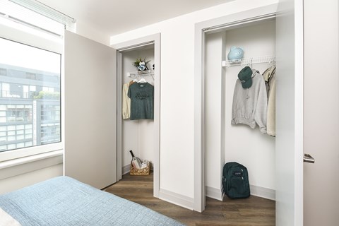 A bedroom with a bed, a window, and a closet with clothes hanging.