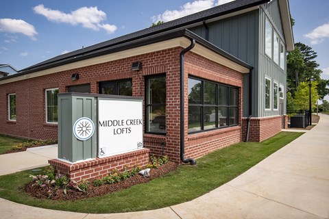 A sign for Middle Creek Lofts is in front of a brick building.