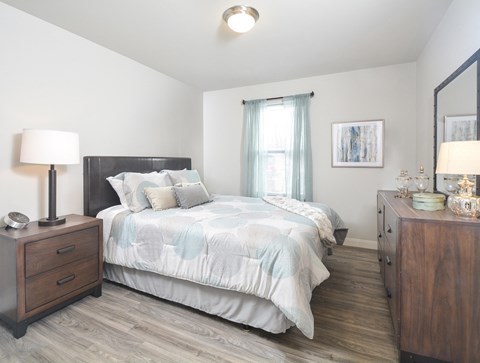 A bedroom with a bed, nightstand, and a wooden dresser.