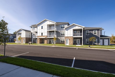 Exterior view of an apartment community with a mix of siding and stone finishes, organized parking, and green landscaping.