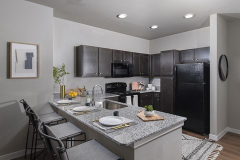 A modern kitchen with a black refrigerator and grey countertops.