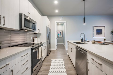 A kitchen with white cabinets and a black and white checkered mat on the floor.