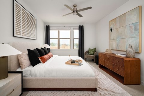 A bedroom with a large bed, a ceiling fan, and a painting on the wall.