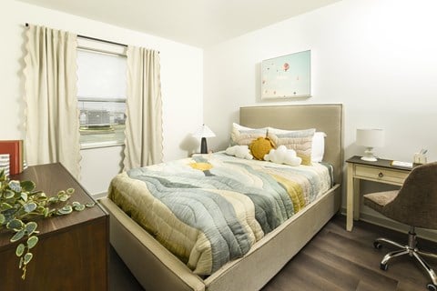 Bright, modern bedroom with a large window, soft neutral curtains, and a stylish upholstered bed paired with a cozy workspace area.