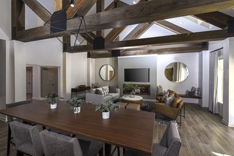 Bright community lounge with tall ceilings, decorative wood beams, and a mix of seating options, including sofas and a large central table for gatherings.