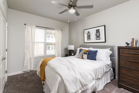 Modern bedroom with a clean layout, featuring a bed with layered bedding, framed wall art, and a window bringing in natural light.