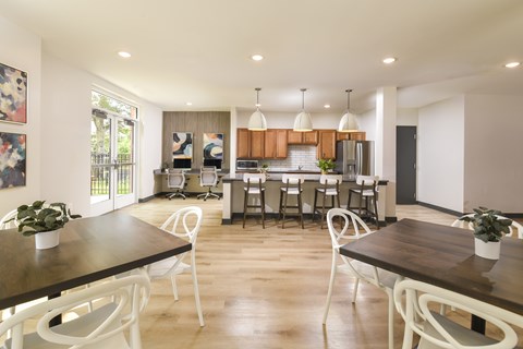 A modern community room with a wooden table and white chairs.