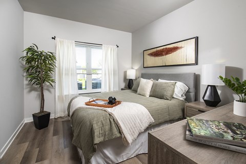 Bright bedroom with a large window, soft curtains, and a neatly styled bed with neutral bedding and accent pillows.