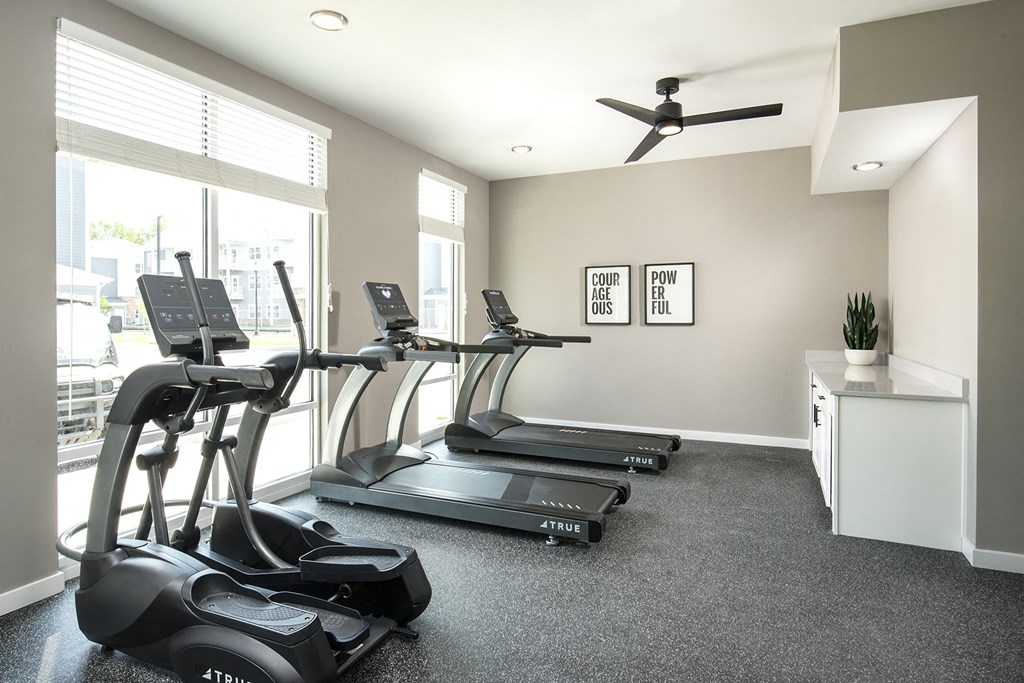 an indoor gym with treadmills and a ceiling fan