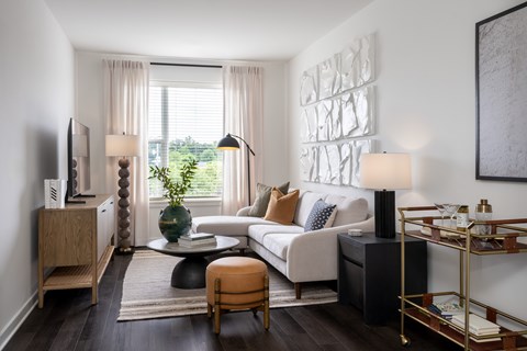 A living room with a white sofa, a wooden cabinet, a glass coffee table, and a large painting on the wall.
