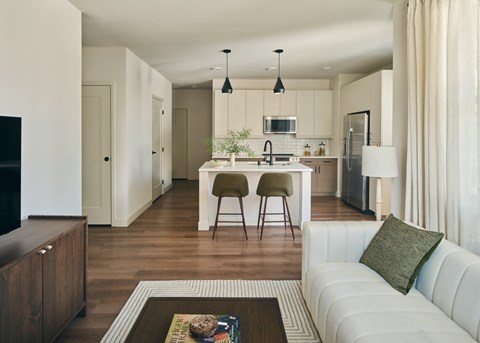 A modern kitchen with white cabinets and a white couch with a green pillow.
