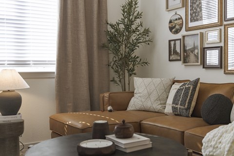 A living room with a brown couch, a table with a lamp and a plant.