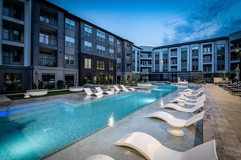 A large swimming pool with lounge chairs is surrounded by apartment buildings.
