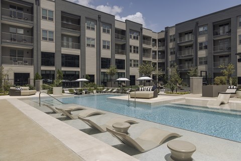 A large swimming pool with lounge chairs and umbrellas in front of apartment buildings.