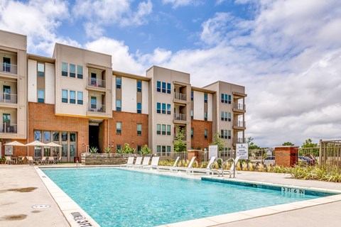 A large swimming pool is in front of apartment buildings.