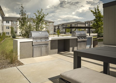 A BBQ grill is in the middle of a concrete patio with seating
