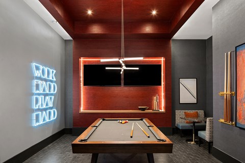 A pool table is in the middle of a room with a neon sign on the wall.
