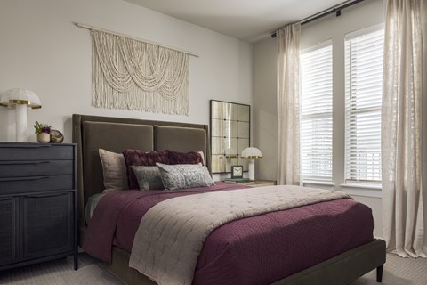 A bedroom with a large bed and a window with white curtains.
