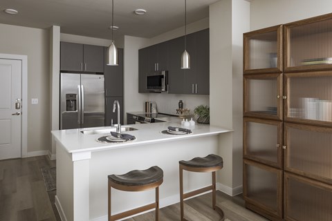 A modern kitchen with a white island and wooden stools.