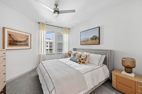 A bedroom with a large bed, a ceiling fan, and a painting on the wall.
