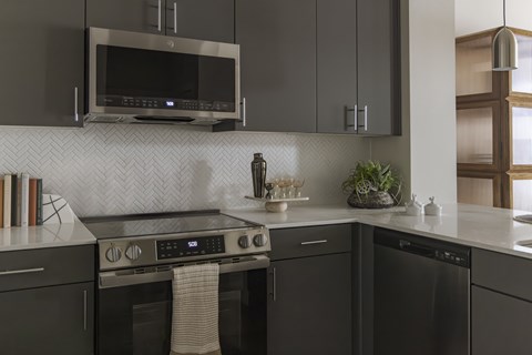 A modern kitchen with dark cabinets and a stainless steel oven.