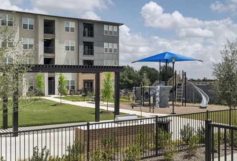A playground with a blue umbrella is in front of a building.