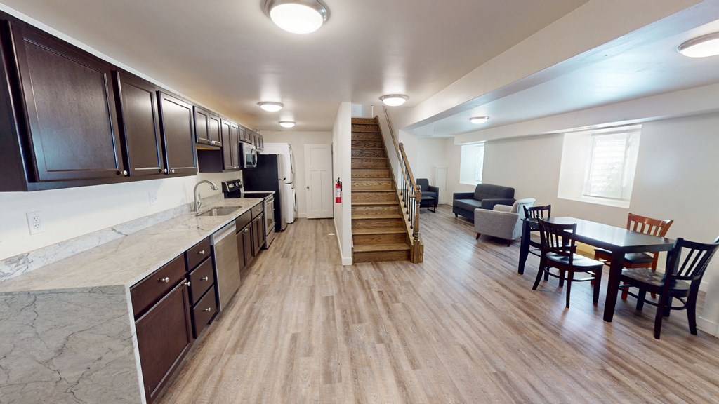 A kitchen with wooden floors and a staircase leading to a living room.
