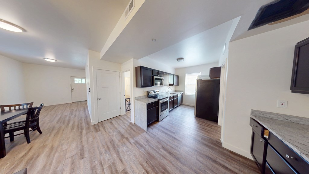 A kitchen with a black fridge and a wooden floor.