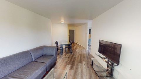 A grey couch sits in a living room with a television on a glass stand.