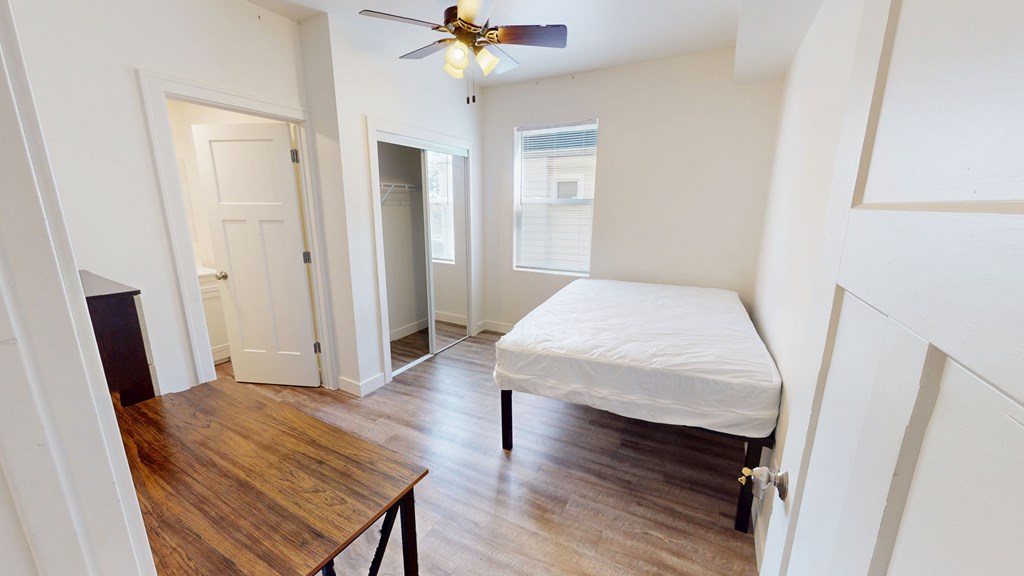 A bedroom with a bed, a table, and a ceiling fan.