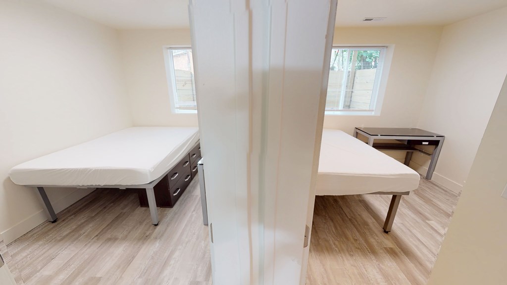 A white bed with drawers is in a room with a white wall and a window.