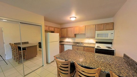 A kitchen with granite countertops and wooden chairs.
