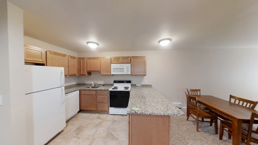 A kitchen with a white refrigerator, a white microwave, a black stove, wooden cabinets, and a wooden dining table.