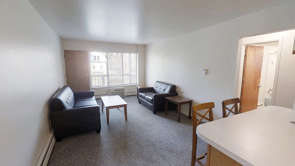 A living room with a black couch, a black chair, a white table, and a brown chair.