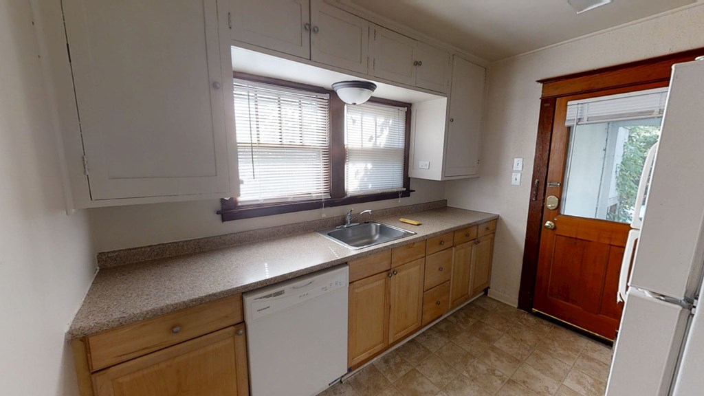 A kitchen with a white dishwasher and wooden cabinets.