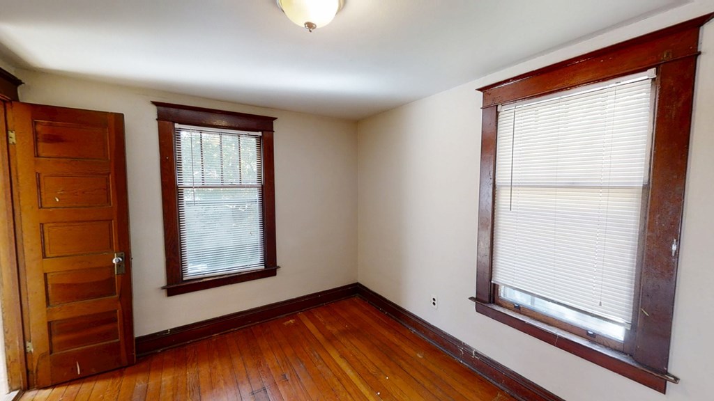 A room with a wooden floor, a door, and a window with blinds.