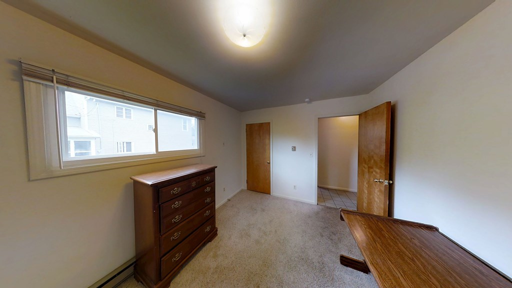 A room with a brown dresser and a window.