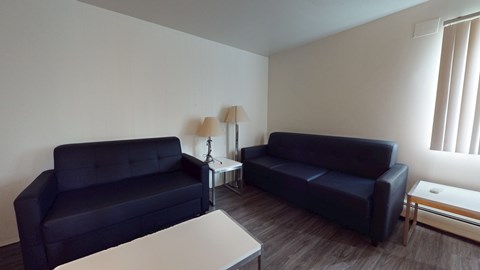 Two black couches in a living room with a white table and a lamp.