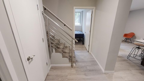 A staircase with a metal railing leads to a bedroom with a bed and a window.