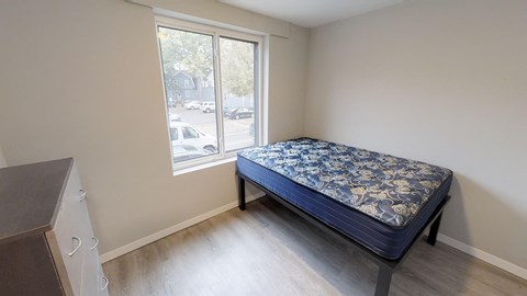 A bed with a blue and white patterned cover is in a room with a window.