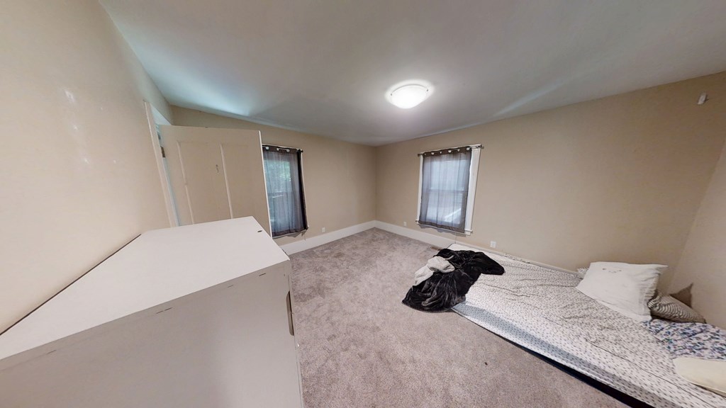 A bedroom with a bed, pillow, and a window with curtains.