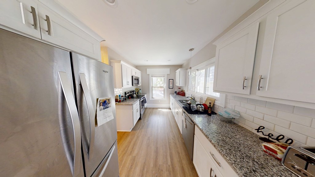 A kitchen with a stainless steel refrigerator and wooden floors.