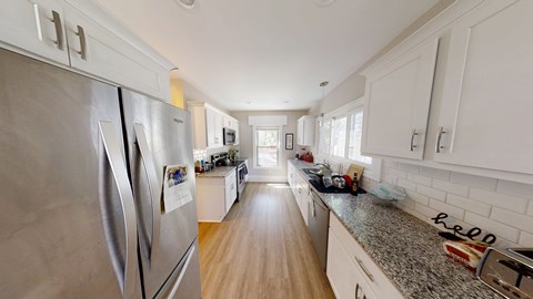 A kitchen with a stainless steel refrigerator and wooden floors.
