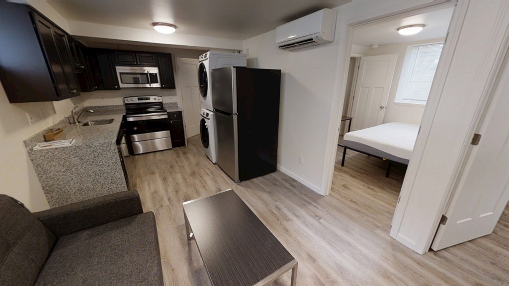 A kitchen with a black fridge and microwave, a black stove, and a grey sofa.