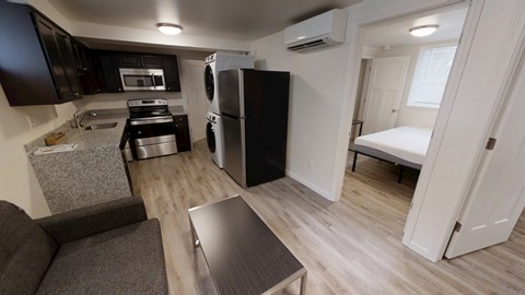 A kitchen with a black fridge and microwave, a black stove, and a grey sofa.