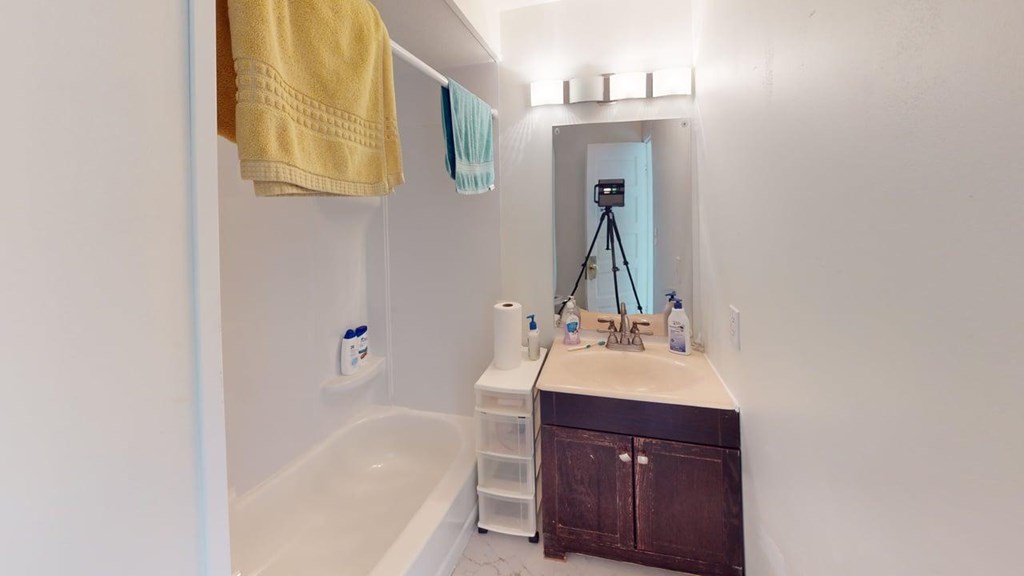 A bathroom with a white tub, sink, and a brown cabinet.