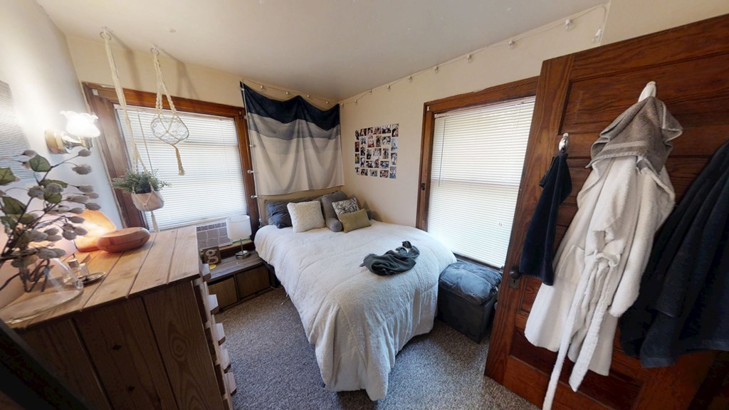 A bedroom with a bed, a wooden cabinet, and a window with blinds.