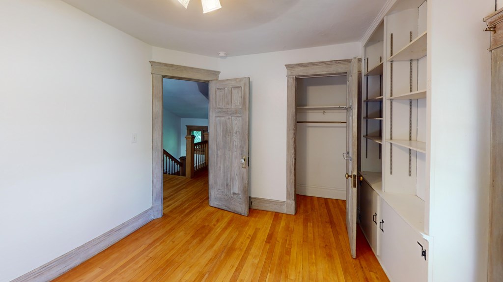 A room with wooden floors and white walls, featuring a large open doorway leading to another room.