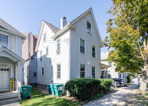 A white house with a green trash can in front of it.